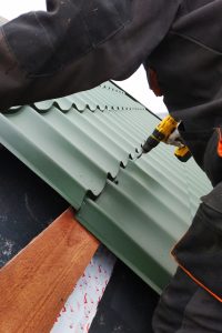 The professional worker works on installation of a roof by sheets of a metal tile